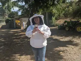 Laura in a white beekeeping suit at a farm.