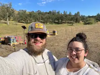 Laura and Bryce wearing beekeeping suits beside their hives.