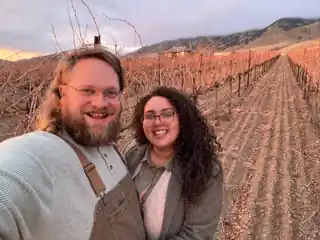 Laura and Bryce smiling together at a vineyard at sunset.