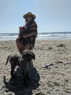Laura holding flowers at our beach proposal, with Weir our Labradoodle beside her.