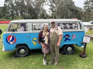 Laura and Bryce beside a blue Grateful Dead Volkswagen bus.