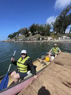 Laura, Bryce and Weir wearing life jackets in a canoe beside a dock.